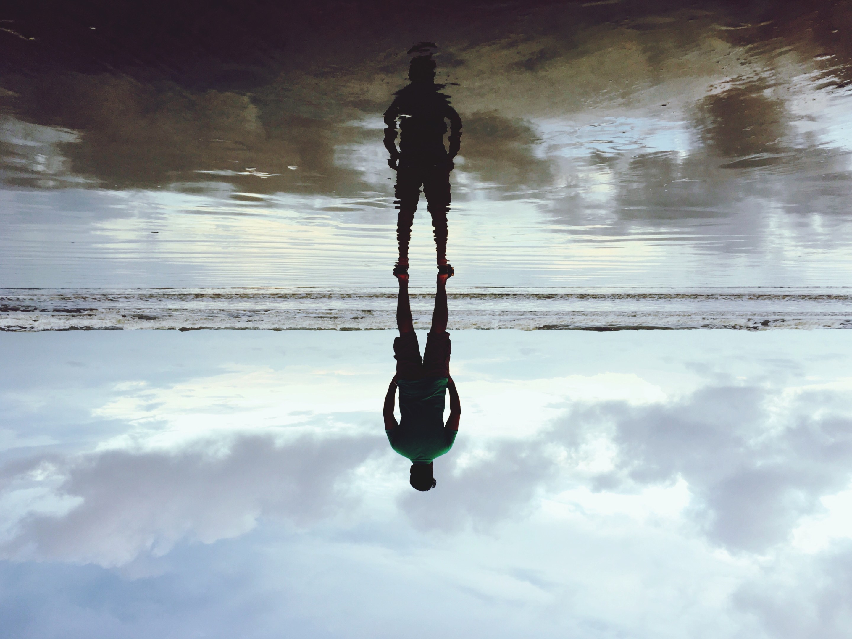 Upside Down Image Of Man Standing At Beach Against Cloudy Sky